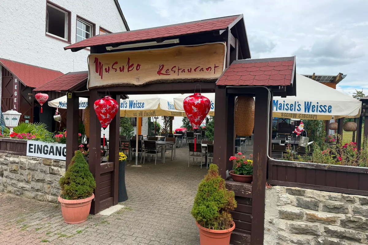 Eingangstor des Musuko mit hölzernem Restaurant-Schild und roten Laternen